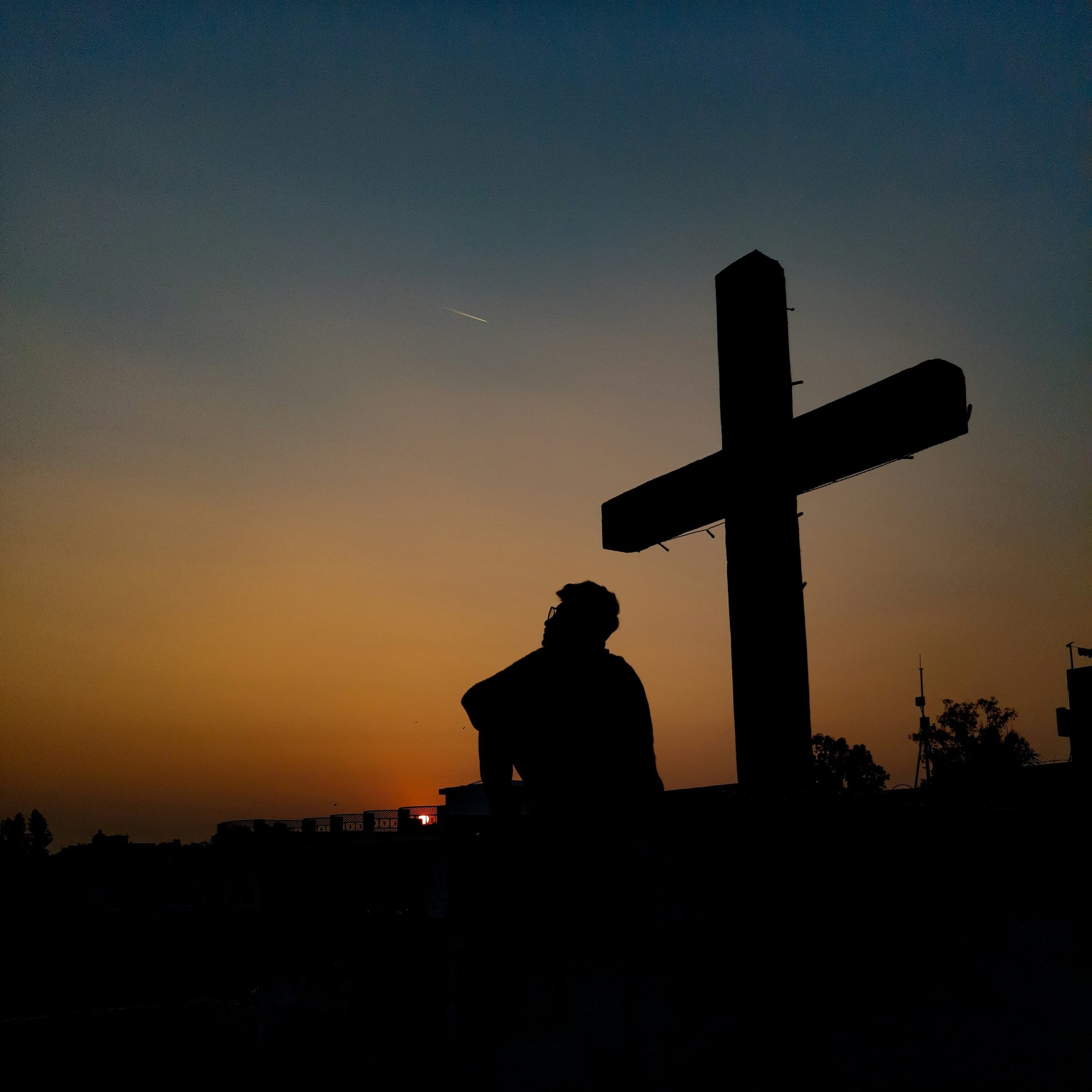 An image of a man sitting beneath a wooden cross