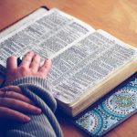 An image of a person reading a Bible which is lying open on a desk.