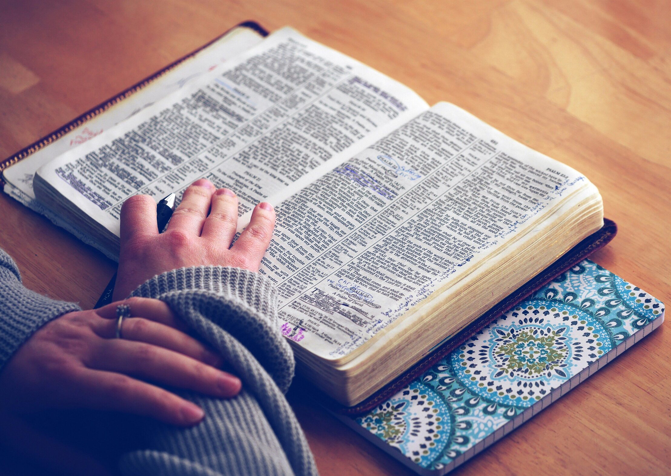 An image of a person reading a Bible which is lying open on a desk.